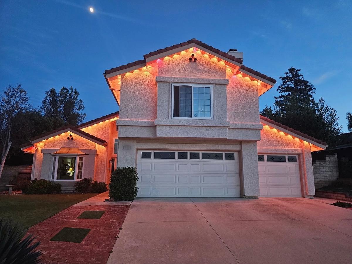 Two-story home at dusk with permanent lights glowing orange and pink under the eaves